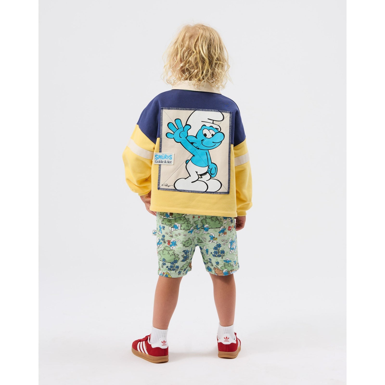 Boy wearing Goldie & Ace x The Smurfs rugby shirt, back view showing Smurf patch