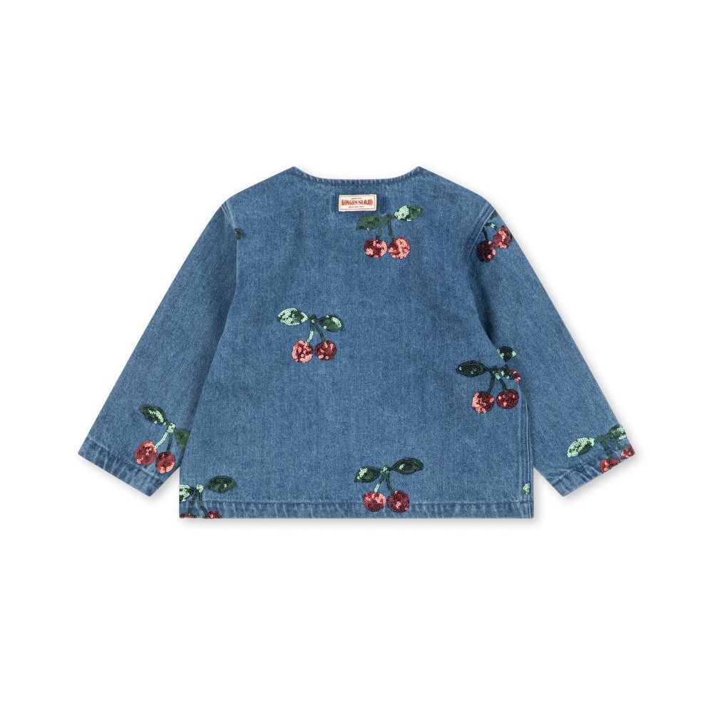 A blue denim long-sleeve top for kids, featuring an all-over cherry print with red cherries and green leaves, laid flat against a white background.